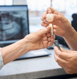 Prosthetist consults an elderly lady in a dental clinic, he shows her a model of a dental implant